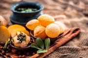 Famous Indian & Asian street food dish i.e. Panipuri snack in a clay bowl along with its flavored spicy water in another clay vessel. Entire consisting raw ingredients present on the surface.