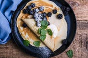Delicious summer treat, healthy vegetarian breakfast with crepes, fresh blackberries and sour cream served in rural cast iron skillet, top view
