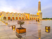 Wide view of Doha Grand Mosque illuminated, mirroring on outdoor marble pavement. Qatar State Mosque, Middle East, Arabian Peninsula in Persian Gulf. Twilight shot. Famous landmark in Doha West Bay.